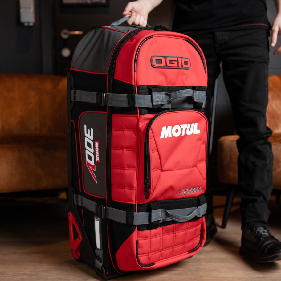 Roter Koffer mit OGIO und MOTUL Logos, von einer Person gehalten.